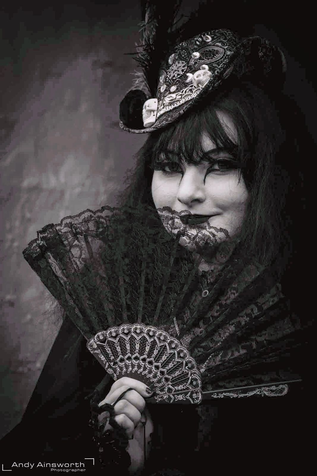 Woman in a decorated mini top hat holding a black lace fan across her face — Whitby Goth Weekend