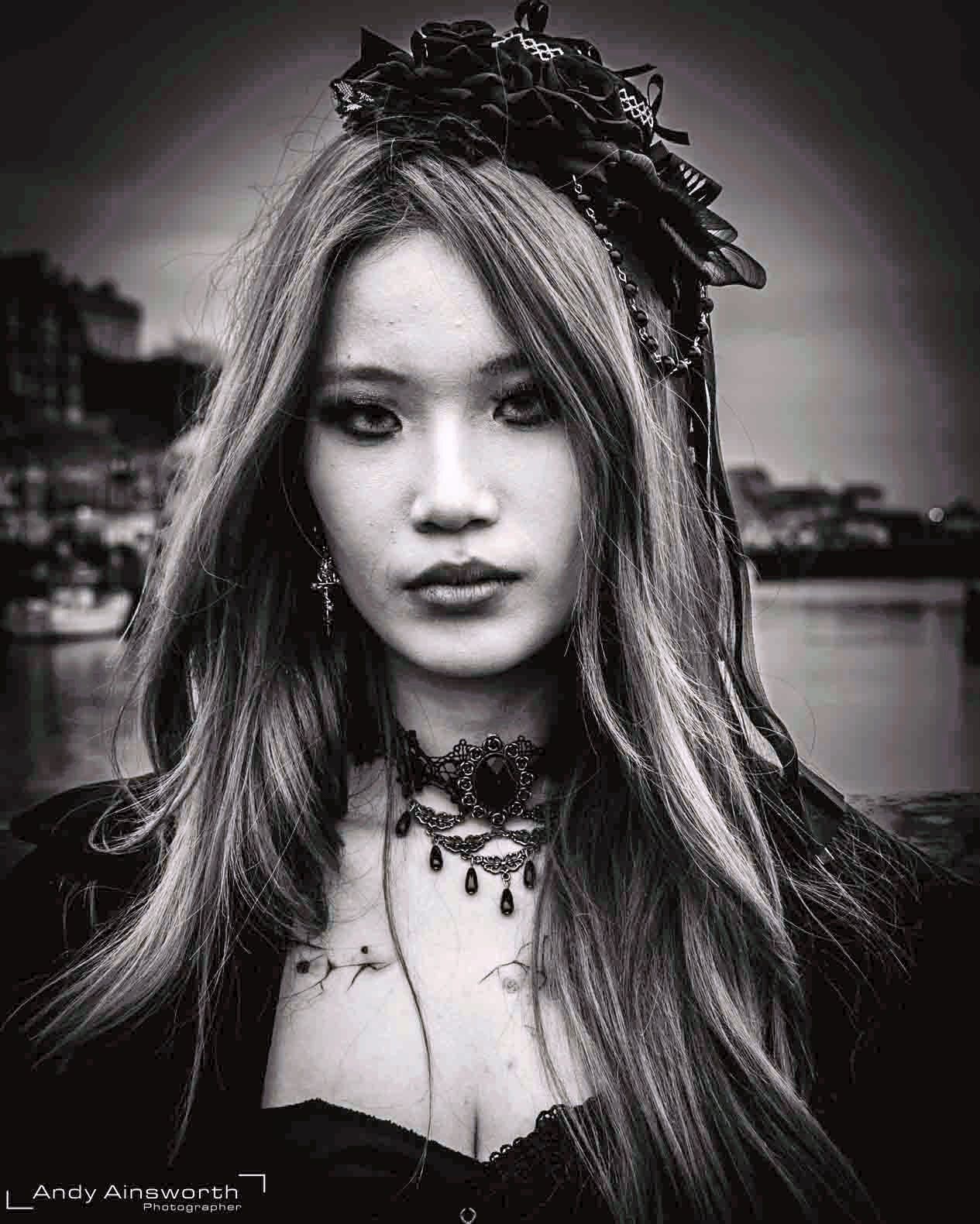 Young woman with long hair beneath a black lace headdress, the harbour behind — Whitby Goth Weekend