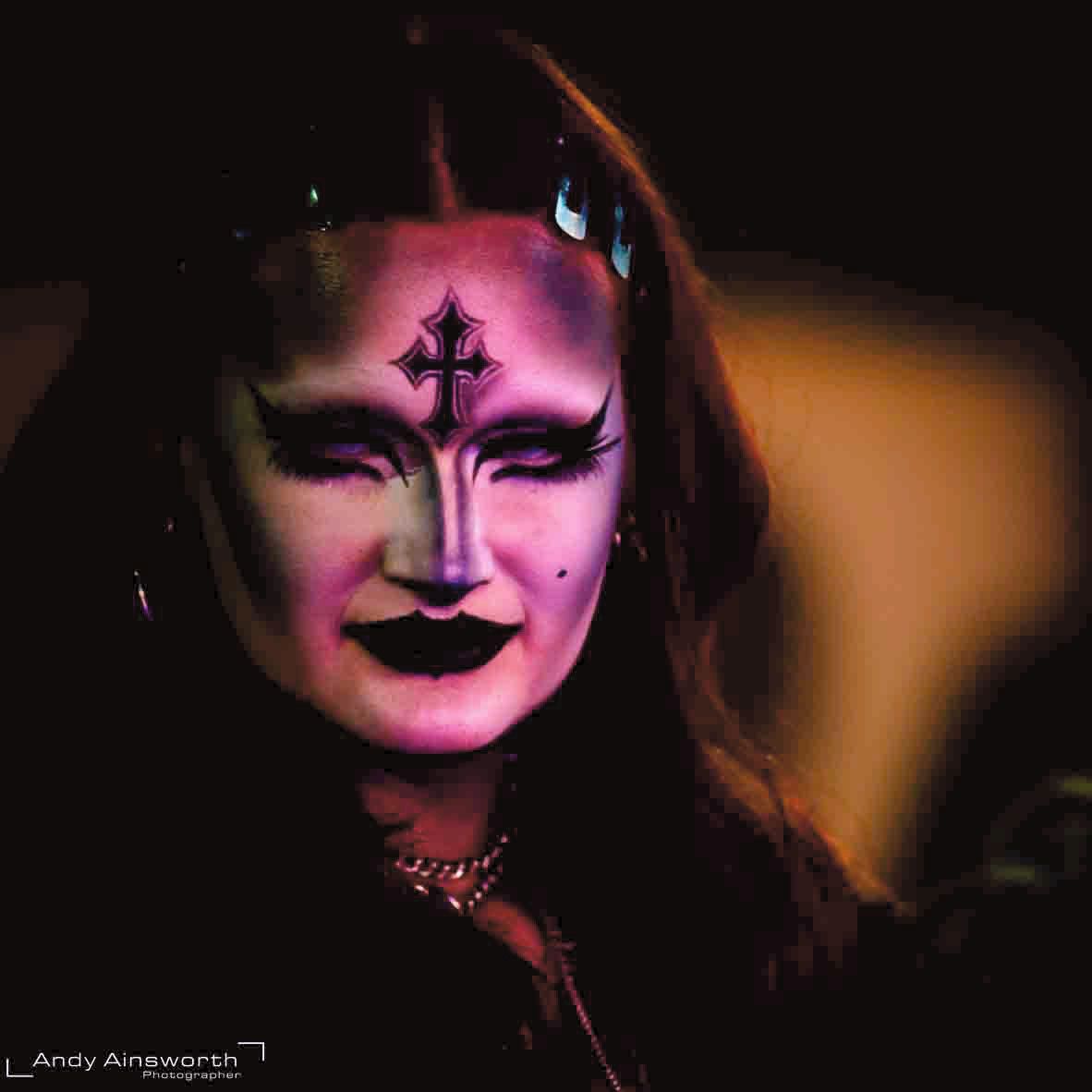 Face painted violet and white with an inverted cross on the forehead, warm light — Whitby Goth Weekend