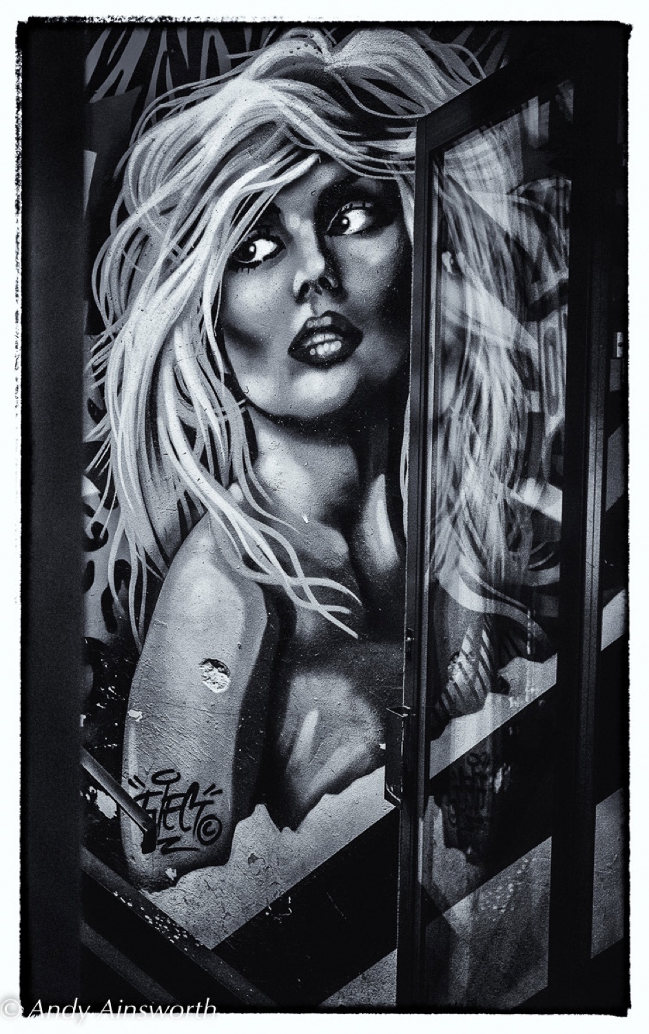 Street art mural of a blonde woman glimpsed through a glass door, Leeds — black and white photograph