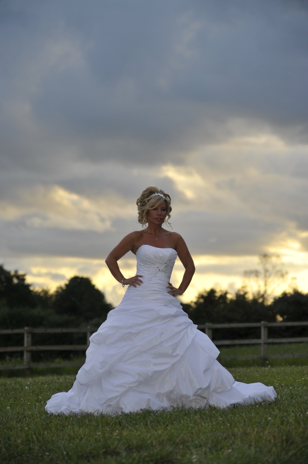 Bride in her gown beneath a dramatic evening sky — full-length portrait at dusk